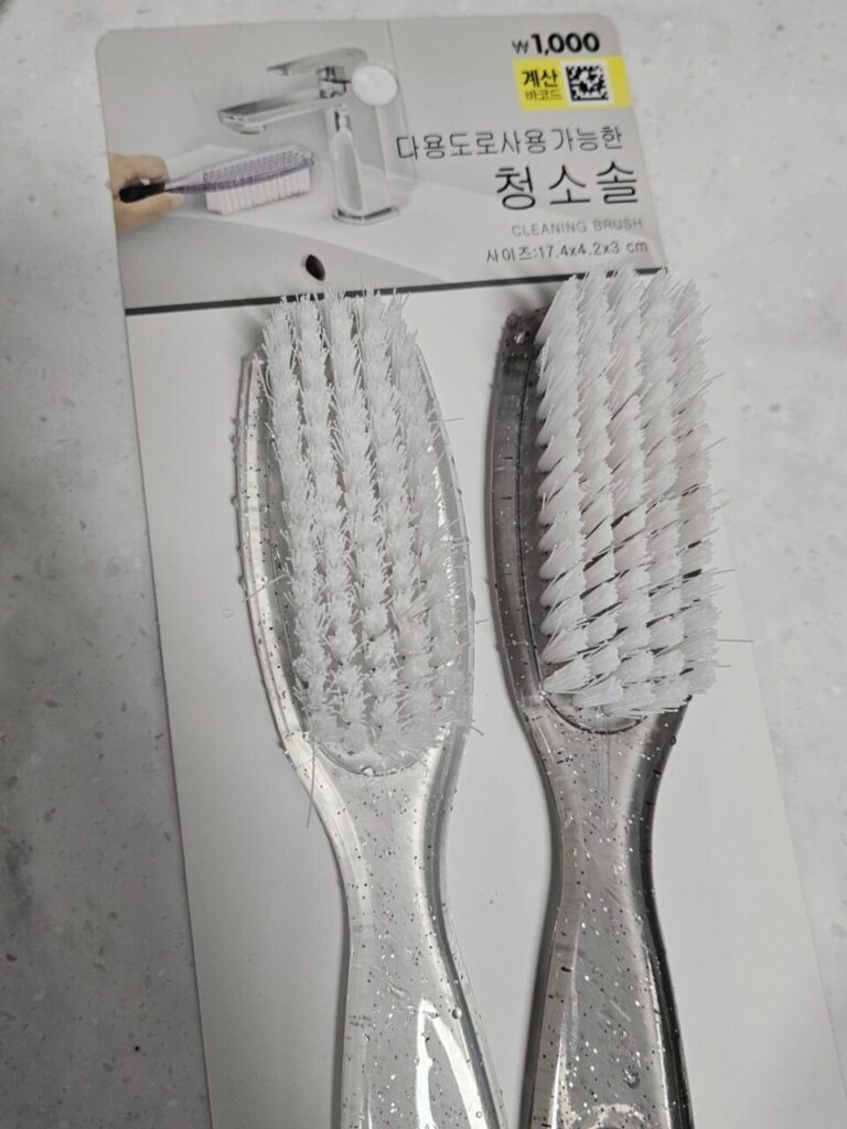 '다용도로 사용 가능한 청소솔'이라는 문구와 함께 1,000원에 판매되는 두 개의 투명한 청소솔 패키지입니다. 부엌이나 욕실 청소에 유용해 보입니다.