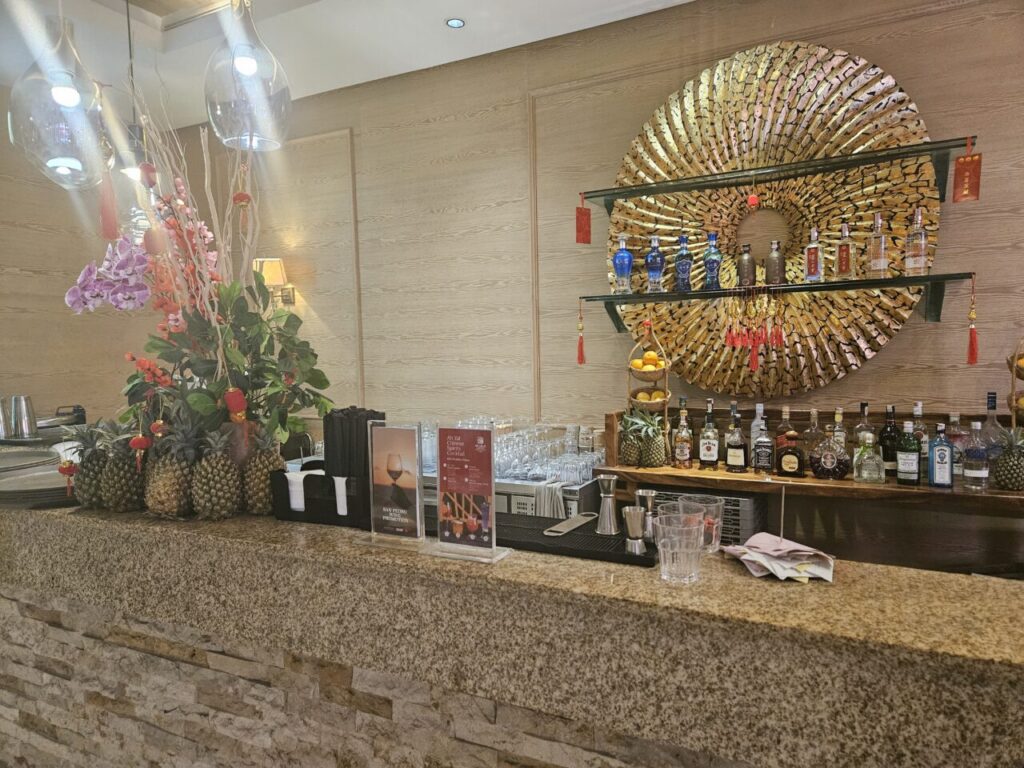 발리 아야나 리조트의 레스토랑 바 카운터. 다양한 주류 병과 칵테일 제조 도구들이 놓여 있고, 황금색 원형 장식이 눈에 띈다.