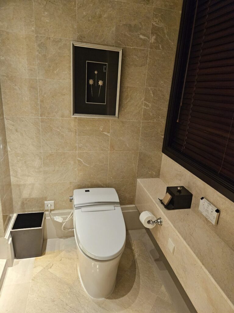 대리석 타일로 마감된 욕실에 설치된 현대적이고 깨끗한 비데 기능이 있는 변기입니다. 벽에는 액자가 걸려 있고, 편의를 위한 용품들이 놓여 있습니다.