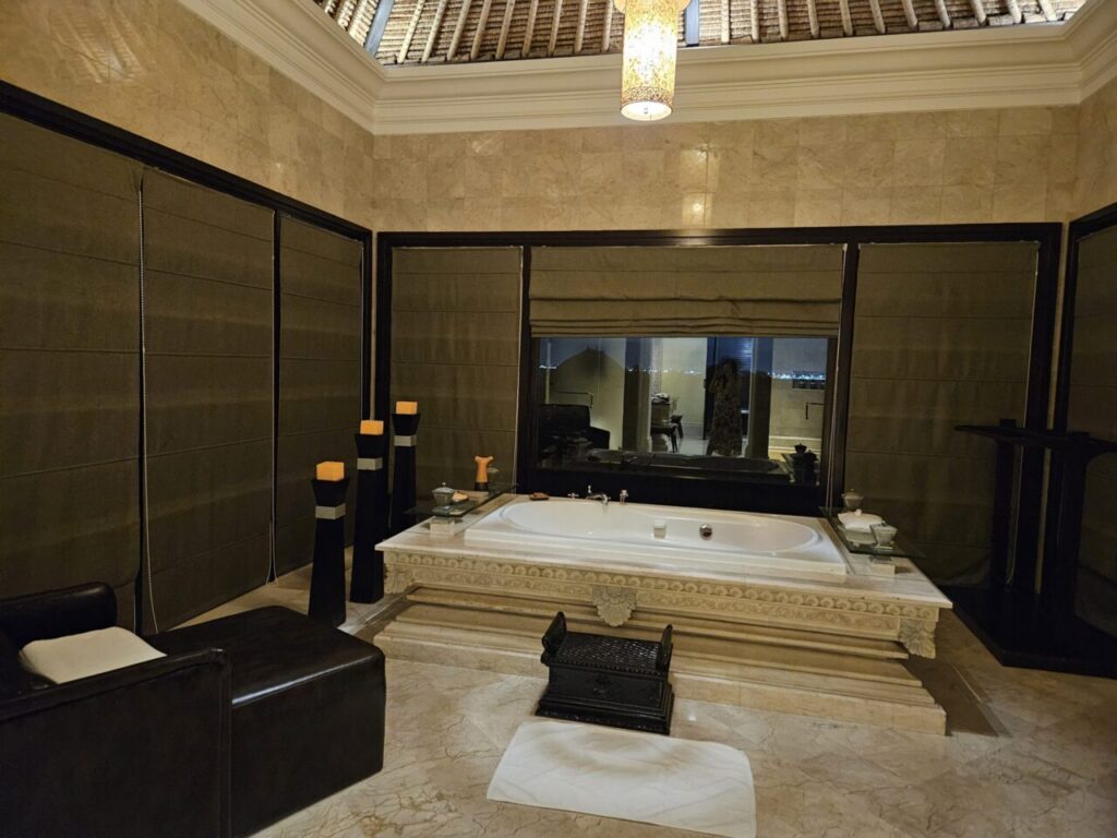 아야나 빌라의 웅장하고 넓은 욕실입니다. 중앙에는 대형 욕조가 자리하고 있으며, 주변에는 세련된 장식품과 은은한 조명이 더해져 고급스러운 분위기를 자아냅니다.