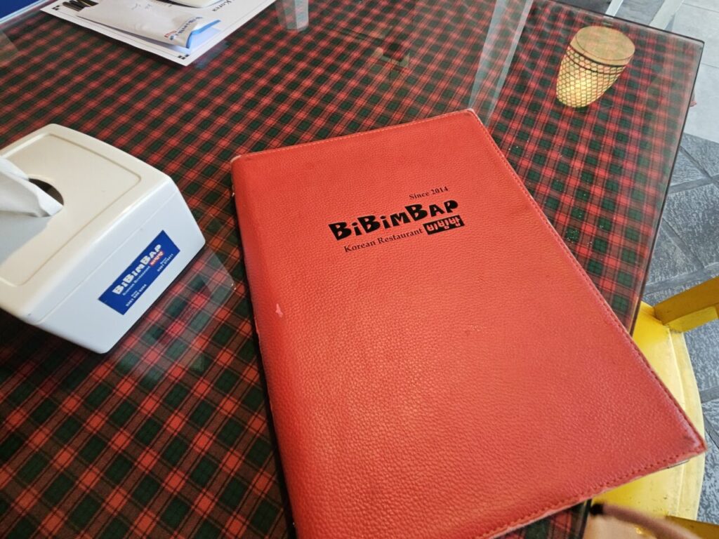 빨간 체크무늬 테이블보 위에 놓인 발리 한식당 비빔밥 메뉴판과 티슈 케이스.