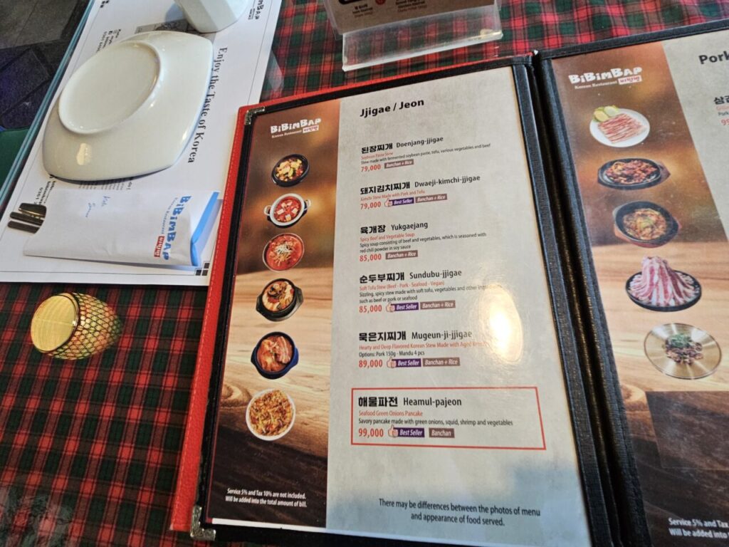 발리 비빔밥 한식당의 메뉴판이 클로즈업되어 있으며, 된장찌개, 김치찌개, 순두부찌개, 해물파전 등 다양한 한식 요리의 이름과 설명, 가격이 자세히 적혀 있다.