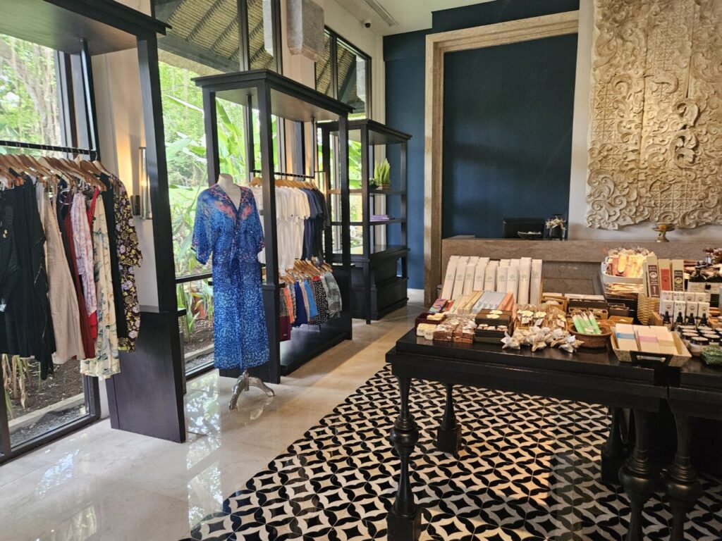 아야나 리조트 상점 내부 전경으로, 아름다운 옷들이 걸려있는 행거와 다양한 기념품들이 진열된 테이블이 보인다.