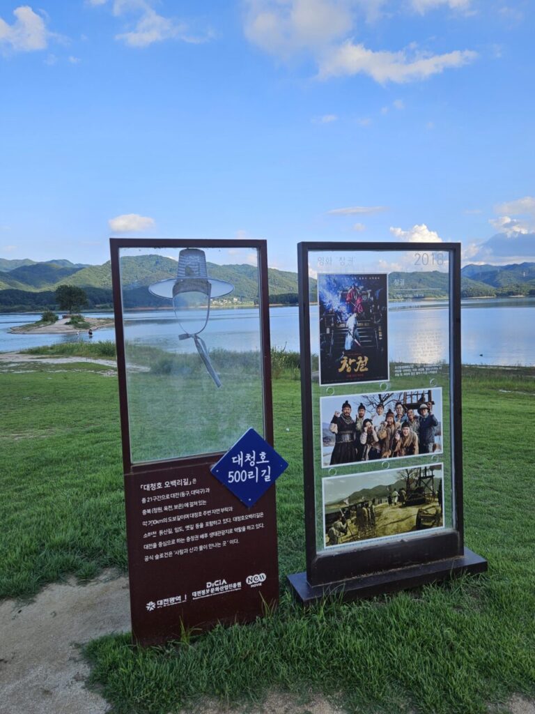 대청호 500리길을 소개하는 안내판과 2018년 영화 '창궐' 포스터가 세워져 있는 대청호변 풍경.