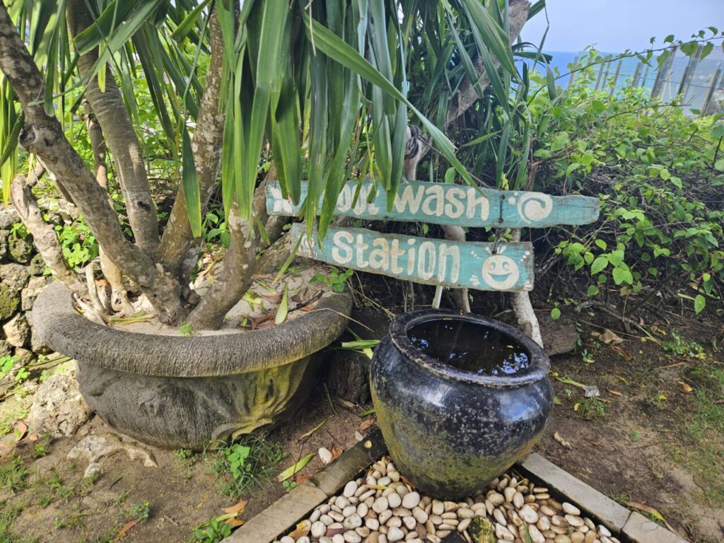 발리 쿠부 비치에 있는 발 씻는 곳 표지판. 큰 검은색 항아리에 물이 담겨 있고 주변에 흰 조약돌이 깔려 있다.