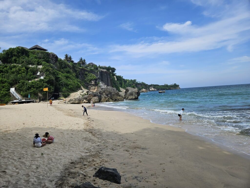 발리 쿠부 비치의 넓은 해변 풍경. 푸른 바다와 모래사장, 그리고 뒤편의 푸른 절벽이 어우러져 아름다운 경치를 자랑한다.