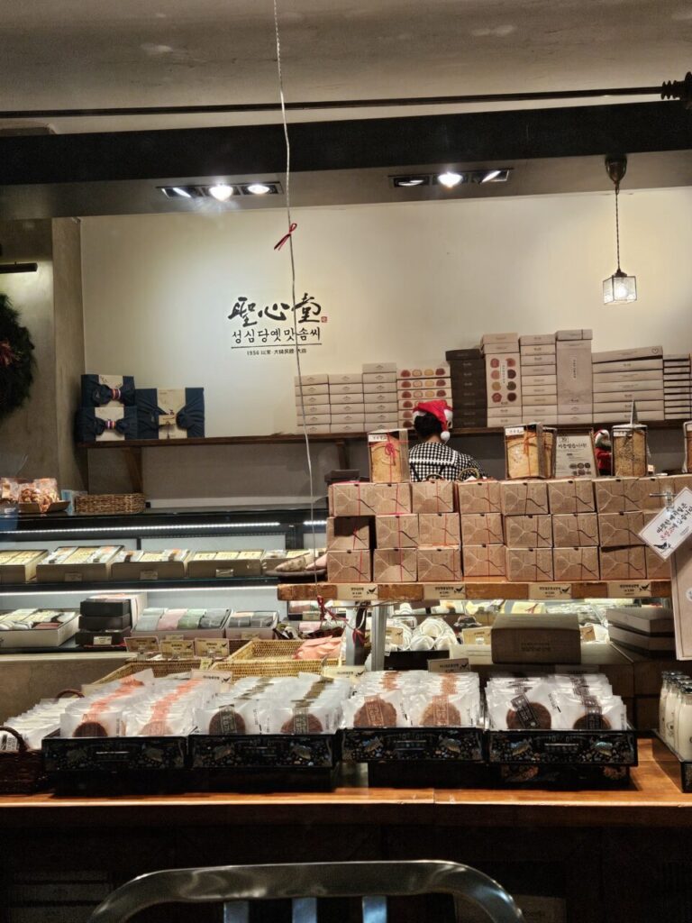 대전 성심당 옛맛솜씨 매장 내부. 다양한 종류의 빵과 과자 선물 세트가 진열되어 있으며, 크리스마스 장식이 보인다.