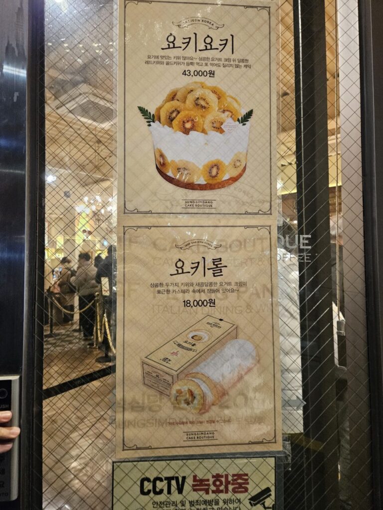 성심당 케이크 부티크의 유리문에 붙어있는 두 개의 포스터입니다. 요거트 크림으로 만든 '요키요키' 홀 케이크(43,000원)와 롤케이크(18,000원)를 홍보하고 있습니다.